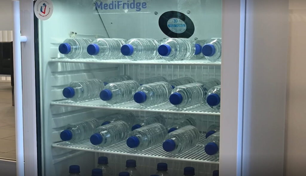  A close up image of a medical fridge stocked with drink bottles laying spaced out on the shelves.