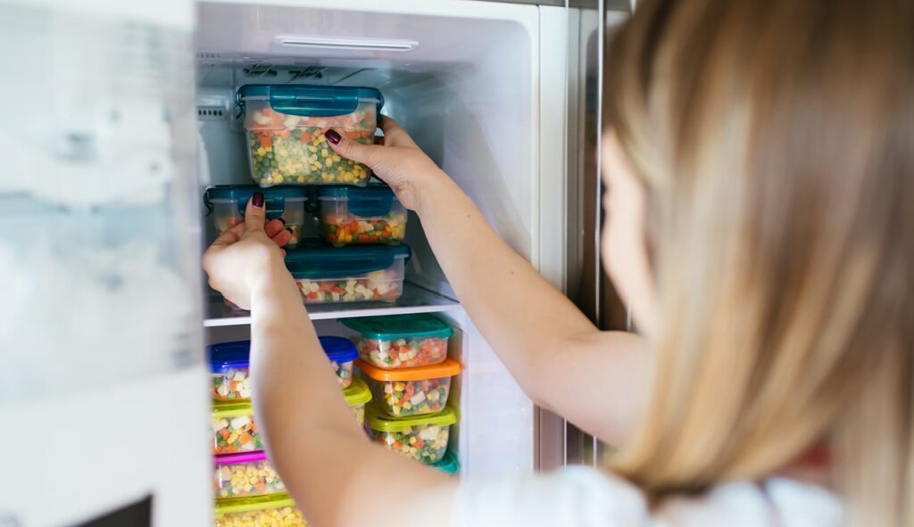 An image of a person putting in a container of air tight food into a freezer.